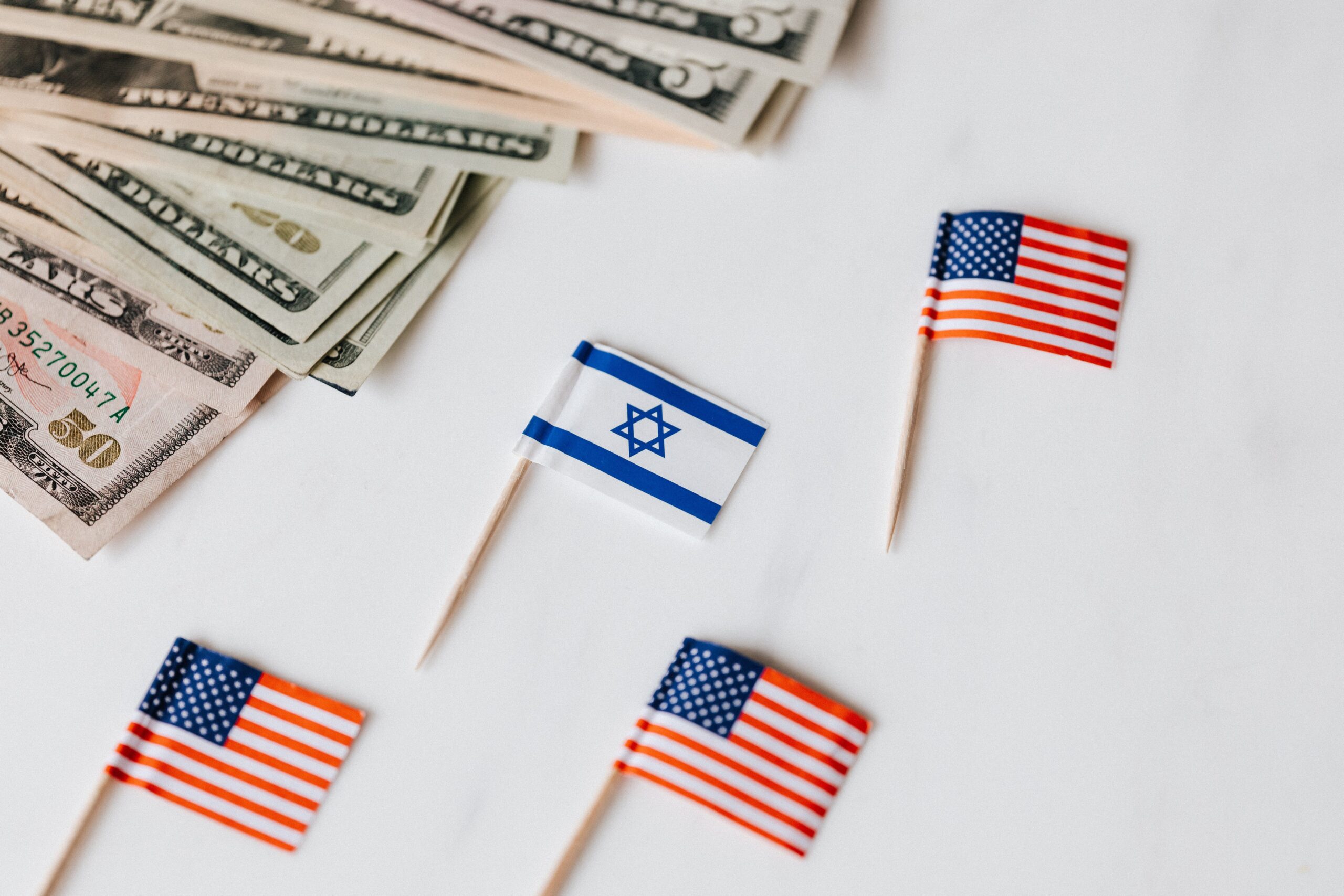 From above closeup of Israeli and American flags on toothpicks and different nominal pars of dollar banknotes on white background
